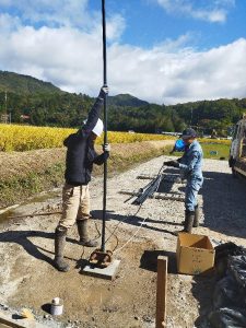 ボーリング井戸に4mのパイプを継ぎ足しながら水中ポンプを降ろしている